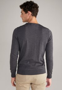 Dunkelgrauer Pullover mit langen Ärmeln, rundem Halsausschnitt und gerippten Bündchen. Glatte Textur, taillierte Passform und über beigen Hosen getragen.