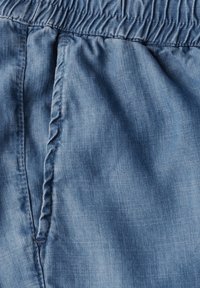 Tessuto blu chiaro con una texture liscia, caratterizzato da un cintura elasticizzata arricciata e dettagli di cucitura sottili. Vista ravvicinata che mette in evidenza il materiale.