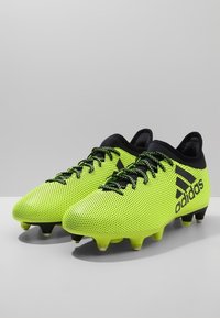 Jasně žluté fotbalové kopačky s texturovaným síťovinovým svrškem, černými akcenty a podrážkou se šesti kolíky pro trakci. Obsahují šňůrky a nízký střih.