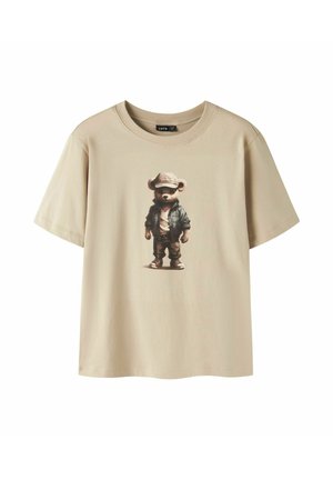 Maglietta beige a maniche corte con una grafica di un orsetto che indossa un cappellino, una giacca, una camicia bianca, pantaloni e scarpe al centro sul davanti.