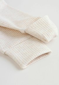 Close-up van opgevouwen beige geribde stoffen mouwen op een lichte achtergrond, met details van textuur en stiksels.