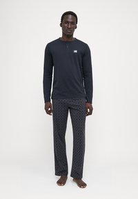 Top negro de manga larga con escote tipo henley y etiqueta; pantalones oscuros grises con un diseño sutil; ajuste relajado, tela suave.