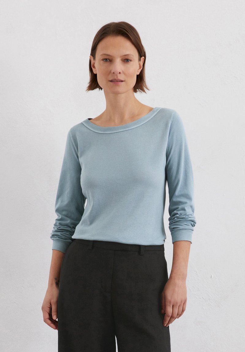 Helles blaues Langarmoberteil mit weitem Bootsausschnitt und gerippten Bündchen, kombiniert mit schwarzen Hosen. Weiches Baumwollmaterial, lässige Passform.