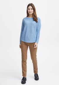 Világoskék textúrájú pulóver kerek nyakkivágással, barna slim-fit nadrággal és fekete platform cipővel párosítva. Egyszerű és modern dizájn.