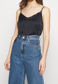 Black satin camisole with lace trim, v-neckline, paired with high-waisted light blue denim jeans featuring wide legs and front pockets.