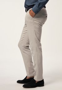 Pantalones de algodón gris claro con corte slim, con bolsillos laterales y un bolsillo trasero. Combinados con mocasines negros, que muestran una textura suave.