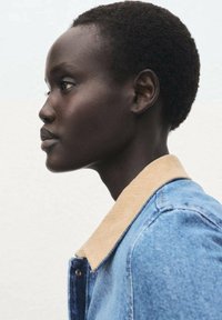 Denim jacket with a tan corduroy collar, featuring a button-up front and contrasting stitching, shown on a model in profile view.