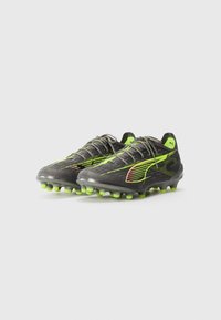 Scarpe da calcio nere con dettagli in verde neon, dotate di una texture rigata, tacchetti appuntiti e un design elegante che presenta un logo sul lato e un sistema di allacciatura.