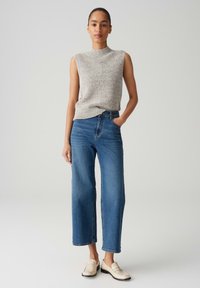 Sleeveless light gray knit top with a high neckline, paired with wide-leg blue denim jeans and cream loafers. Simple design and relaxed fit.