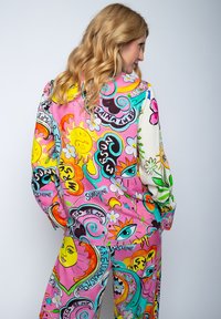 Kolorowy dwuczęściowy zestaw z różowym tłem i wielokolorowymi wzorami słońca, oka oraz kwiatów. Materiał wydaje się lekki i ma luźny krój.