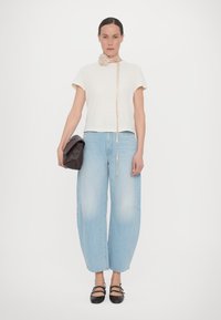 Light beige shirt with short sleeves, paired with loose, light blue jeans. Accessories include a floral neck piece and a dark brown clutch.