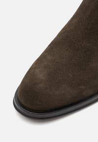 Pointe de chaussure en daim marron avec forme arrondie et semelle noire sur fond blanc.
