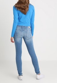 Top azul de manga larga combinado con jeans ajustados de un azul claro con un ligero desgaste y una cintura de altura media; zapatillas blancas completan el conjunto.