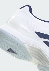 Chaussure de sport blanche avec une tige texturée, des accents bleu marine et une semelle en caoutchouc à motifs. Dotée d'un talon lisse et brillant pour la stabilité.