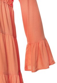 Manica lunga di un vestito corallo con polsini a campana arricciati e tessuto a strati arricciato visibile vicino alla vita e alla manica.