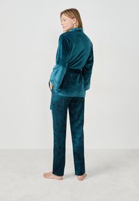 Szlafrok z aksamitu w kolorze zielonkawoniebieskim z szerokimi rękawami, w parze z zielonkawoniebieskimi spodniami z ciemnym kwiatowym wzorem. Miękka tekstura, wiązany w talii, o luźnym kroju.