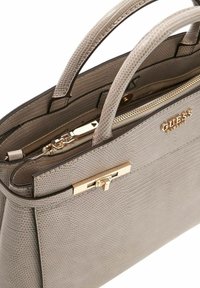 Sac à main texturé gris avec double poignée, ferrures argentées, compartiment zippé et accent logo doré. Finition en cuir lisse.