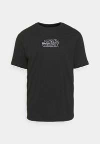 Musta puuvillapaita, jossa on valkoinen "STAR WARS" -logo, pyöreä pääntie, lyhyet hihat ja normaali istuvuus ilman lisäkuvioita.