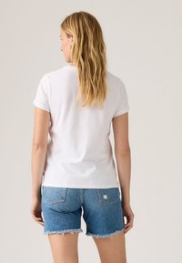 Λευκό βαμβακερό κοντομάνικο μπλουζάκι φορεμένο με μπλε τζιν σορτς με φθαρμένες άκρες και πίσω τσέπες. Απλός σχεδιασμός, χωρίς ορατά μοτίβα.