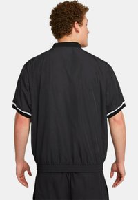 Giacca leggera nera con maniche corte, vita elastica e dettagli a strisce bianche. Tessuto morbido con un design classico.