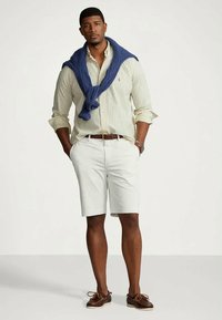 Λευκά σορτς, πουκαμίσα με ρίγες και μπλε πουλόβερ που κρέμεται στους ώμους. Καφέ παπούτσια για βάρκα. Καθημερινό ντύσιμο με χαλαρή εφαρμογή.