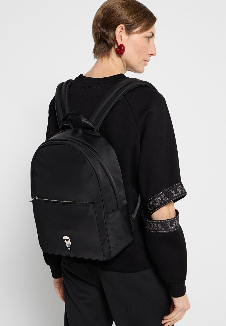 Sac à dos en nylon noir avec une texture lisse, une forme arrondie, une poche zippée à l'avant et un détail de personnage de dessin animé remarquable à l'avant.