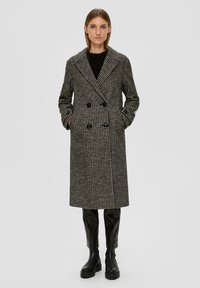 Dubbelzijdige jas in zwart-wit houndstoothpatroon, met een brede kraag, zijzakken en knopenaccenten. Gecombineerd met zwarte leren broek.