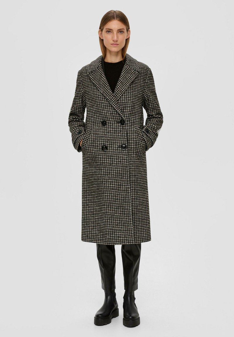 Dubbelzijdige jas in zwart-wit houndstoothpatroon, met een brede kraag, zijzakken en knopenaccenten. Gecombineerd met zwarte leren broek.