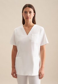 Maglia da lavoro bianca con scollatura a V, maniche corte, tasca sul petto e due tasche frontali. Realizzata in un tessuto liscio e leggero.