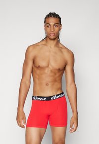 Rote Boxer-Briefs mit einem schwarzen elastischen Bund, der weiße Schriftzüge trägt. Glatte Textur, enganliegendes Design, mittellange Oberschenkel.