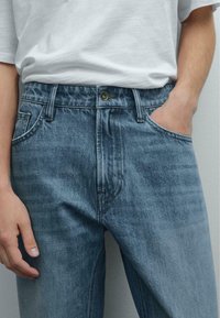 Lichtblauwe spijkerbroek van denim met een vervaagde afwerking, met een knoopsluiting aan de voorkant, riemlussen en zijzakken. De textuur is soepel en stevig.