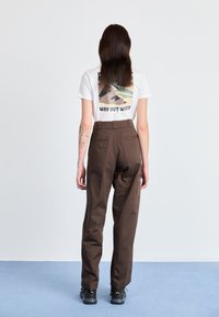 Calças castanhas de cintura alta com frente lisa e bolsos traseiros. Combinadas com uma t-shirt branca com estampado gráfico multicolorido.