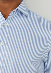 Chemise rayée bleu clair et blanc en tissu à texture lisse, dotée d'un devant avec boutons et d'un col classique.