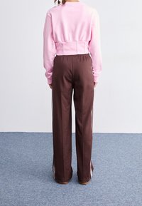 Avklippt rosa sweatshirt i kombination med bruna träningsbyxor med vita sidostråkar. Mjuk tyg med avslappnad passform och elastisk midja.