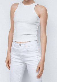 Camiseta blanca de canalé con un alto escote y diseño sin mangas, combinada con pantalones blancos. El tejido parece suave y ajustado.