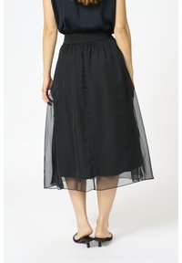 Gonna nera di media lunghezza realizzata in chiffon trasparente, con una fascia elasticizzata in vita e una fodera liscia. Caratterizzata da un design fluido e leggera trasparenza.