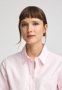 Ljusrosa skjorta med knappar och klassisk krage, med en diskret logostickning och slät bomullstextur.