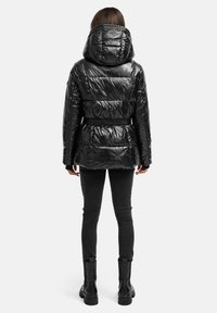 Sort pufferjakke med en blank finish, oversize hætte, indsnøret talje og tekstureret stof, parret med sorte slim-fit jeans og støvler.