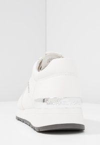 Sneaker bianca con tomaia in pelle liscia, accentata da un dettaglio argento di Michael Kors sul tallone, suola intermedia bianca texturizzata e suola in gomma.