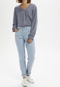 Grå langærmet bluse med V-hals, sat sammen med lyseblå opsmøgede jeans og hvide sneakers. Blødt stof og afslappet pasform.