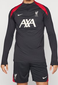 Schwarzes Langarm-Sportoberteil mit roten Akzenten, ausgestattet mit hohem Kragen und Reißverschluss, kombiniert mit schwarzen Shorts und weißem Nike-Logo sowie L.F.C.-Emblem.