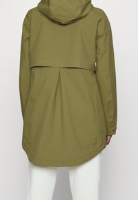 Oliwkowa kurtka z kapturem z plisowanym tyłem i bocznymi zapięciami. Posiada zaokrąglony dół i widoczne logo marki na dolnym prawym rogu.