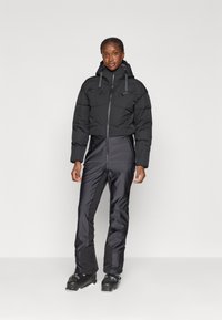 Must have kapuutsiga must voodriga jakk, koos sobiva musta suusapüksega. Tekstuuriga kangas, millel on siledad aktsendid ja sujuv disain.