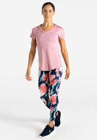 Camiseta de cuello en V rosa claro, combinada con leggings navy que presentan un colorido patrón floral en rosa, blanco y teal, complementados con zapatillas negras.