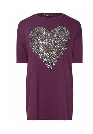 Violetti t-paita lyhyillä hihoilla, jossa on suuri hopeinen paljetti sydänkuvio edessä. Sileä kangas, rento malli.