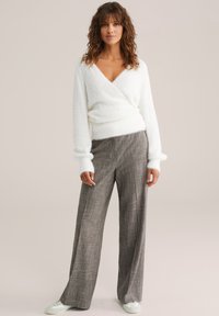 Valge karvane salli süda, hallide ruuduliste laiade pükste ja helesiniste sneaksidega. Pehmed tekstuurid, mugav lõige ja V-kujuline dekoltee.