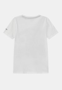 Camiseta de algodón blanca de manga corta, con cuello redondo y una etiqueta en la manga izquierda. Textura suave, diseño simple y color sólido.