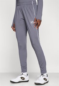 Šedé športové nohavice s elastickým pásom, bielym bočným pruhom a logom Under Armour, vyrobené z ľahkého a priedušného materiálu.