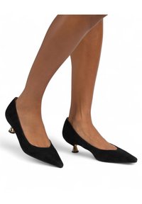 Décolleté in suede nero con punta affusolata e tacco basso affusolato, caratterizzati da un accento metallico alla base del tacco. Texture liscia e design elegante.
