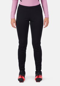 Schwarze Sporthosen mit enganliegendem Design, aus dehnbarem Material, ausgestattet mit Nähten für Bewegungsfreiheit, kombiniert mit rot-schwarzen Skischuhen.